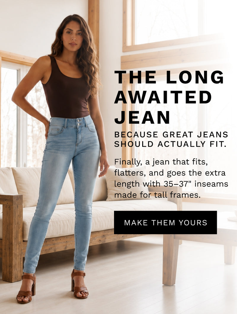 A woman modeling light-wash blue jeans in a bright indoor room, paired with a dark brown tank top and brown heeled sandals. Large text on the right reads 'THE LONG AWAITED JEAN' with supporting copy about fit and a button that says 'MAKE THEM YOURS'.